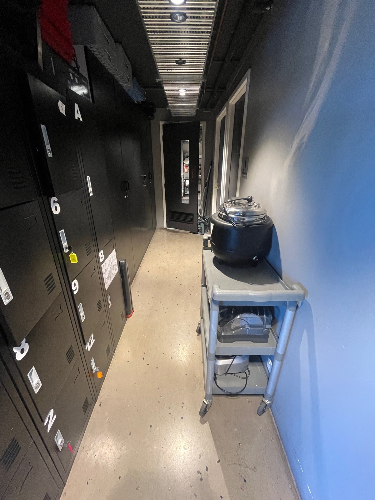 From preceding door facing left. Lockers on left wall and trolley on right wall obstructing hallway ahead.