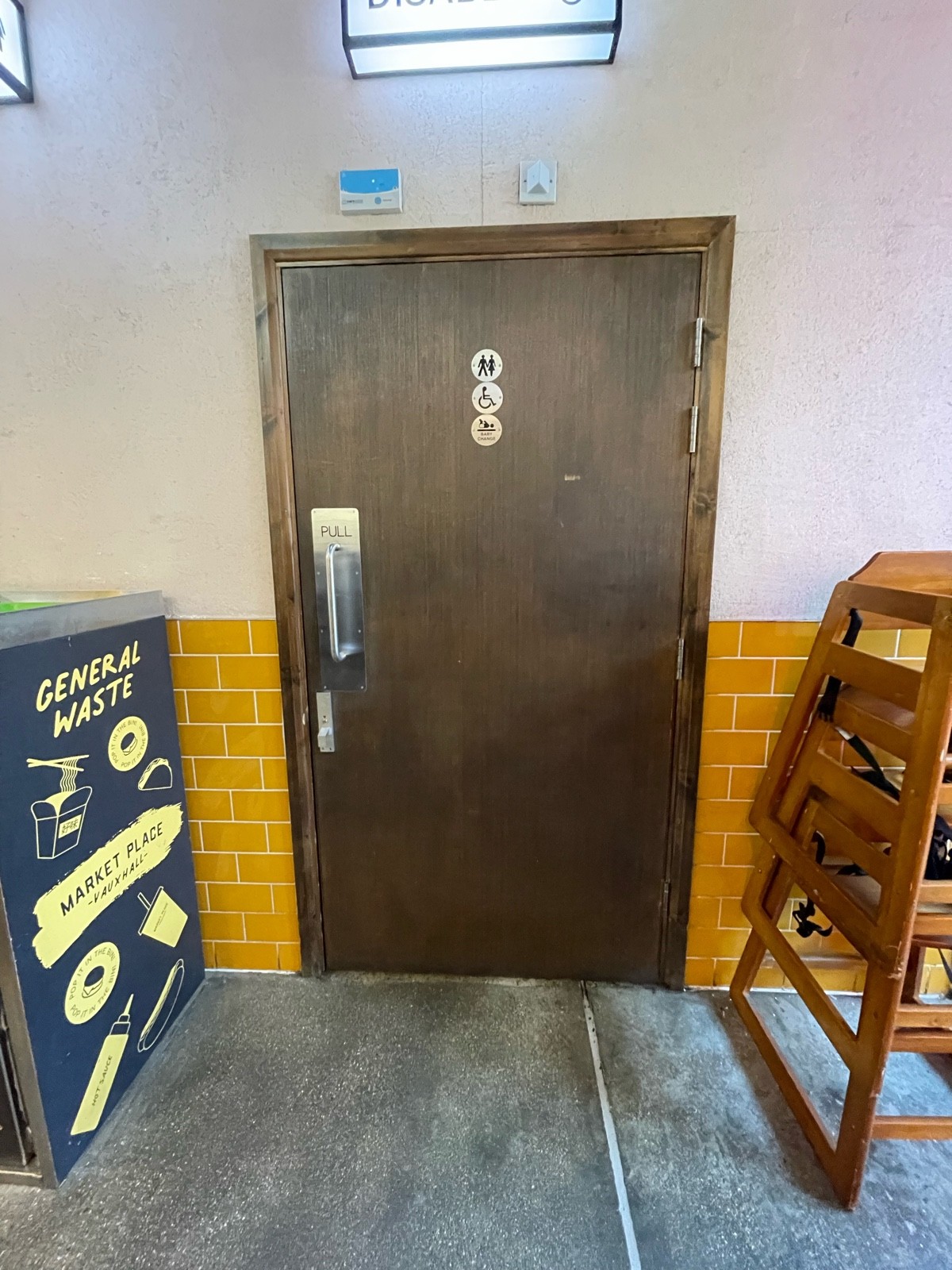 Facing toilet door. Pull sliver handle on left to open.