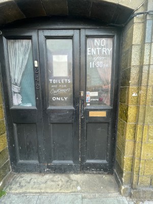 Black glass and wooden doors ahead. Push from centre to open. Doorbell for assistance on left.