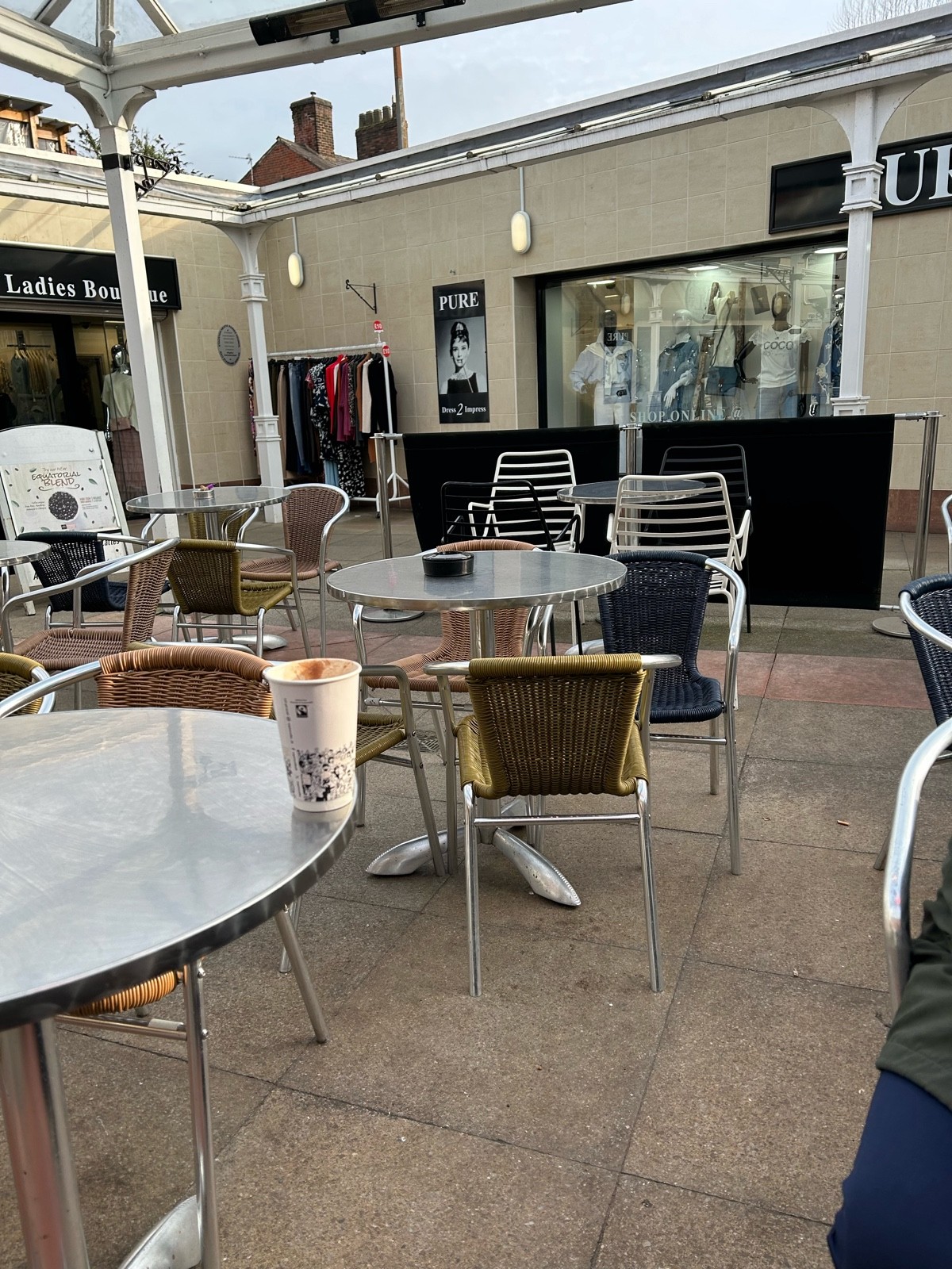 Table/chairs undercover, not much space in between, metal poles with banner at the side/ back of seating with light gap to wheel through Outside shops
