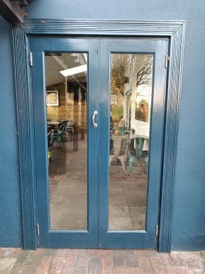 From left of entrance, looking straight. Glass doors with blue wooden frame. Pull silver handle in middle to open.