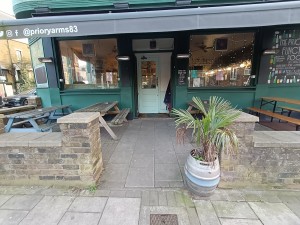 From street, facing venue. Opening ahead. Planter on right. Path in middle to doorway at back.