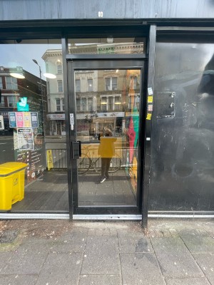 Glass door with black frame ahead. Push black metal handle on left to open.