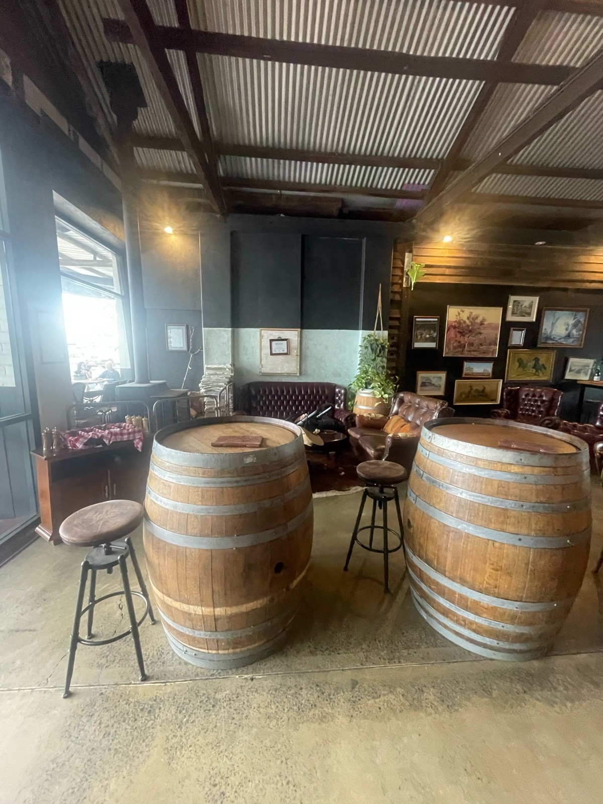 Bar stools around wine barrel tables. Couches and armchair area behind