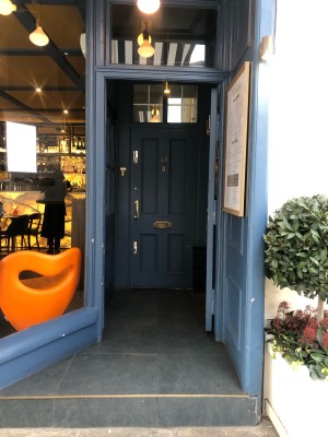 Step up before first preceding door. Blue framed glass door. Push from left to open.