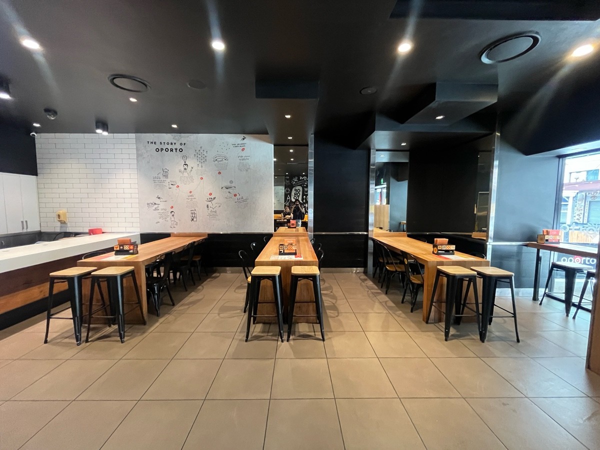 From before counter facing right. Tables and chairs along wall ahead. High table and backless stools on right wall.