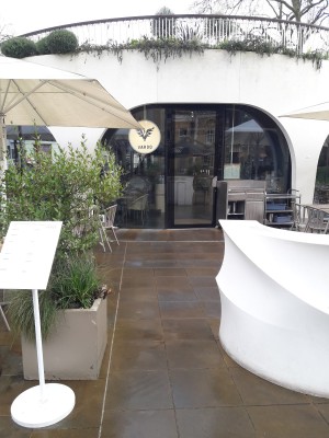 From pavement facing venue. Welcome desk on right. Path in centre to door. Planter on left.