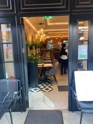 Glass door with black frame ahead. Push to open from right. Outdoors seating to both sides of door.