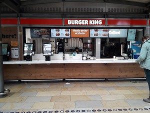 From station facing venue. Opening ahead. Counter at the back. Self ordering screens along back left.
