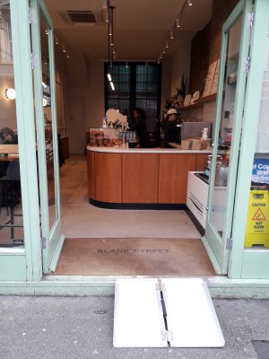 Glass doors with green frames. Push in centre to open. Doormat behind.