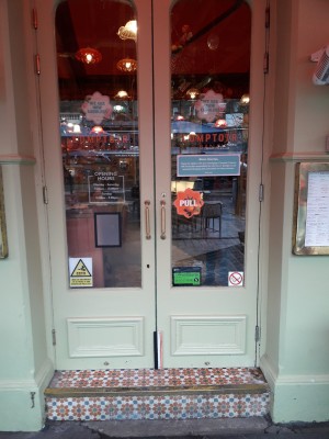 Glass doors with green frames. Pull from metal handles at centre to open. One step up at foot of door.