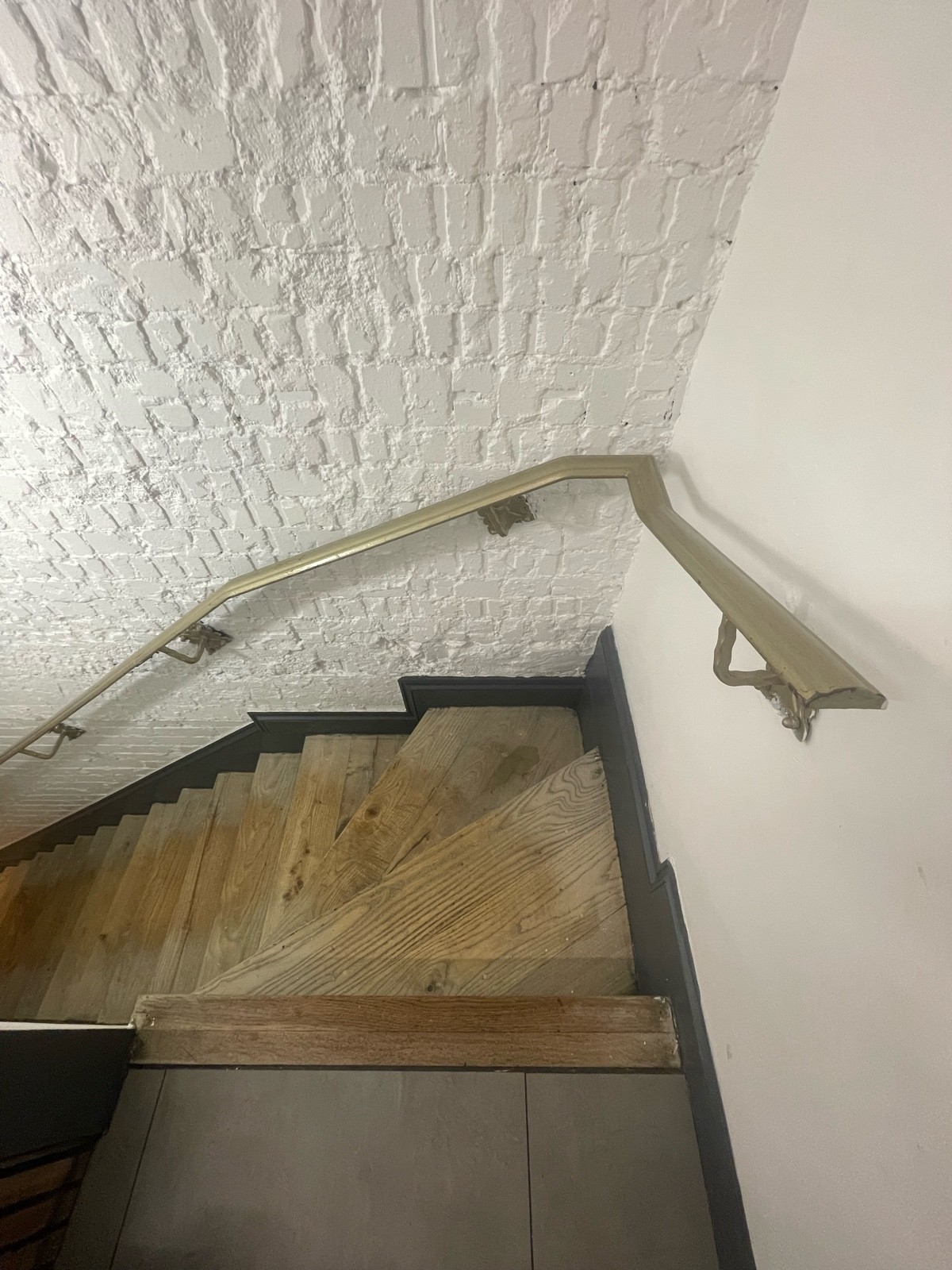 From opening facing straight. Two steps of full flight of stairs down curving towards left ahead. Metal handrail to right.