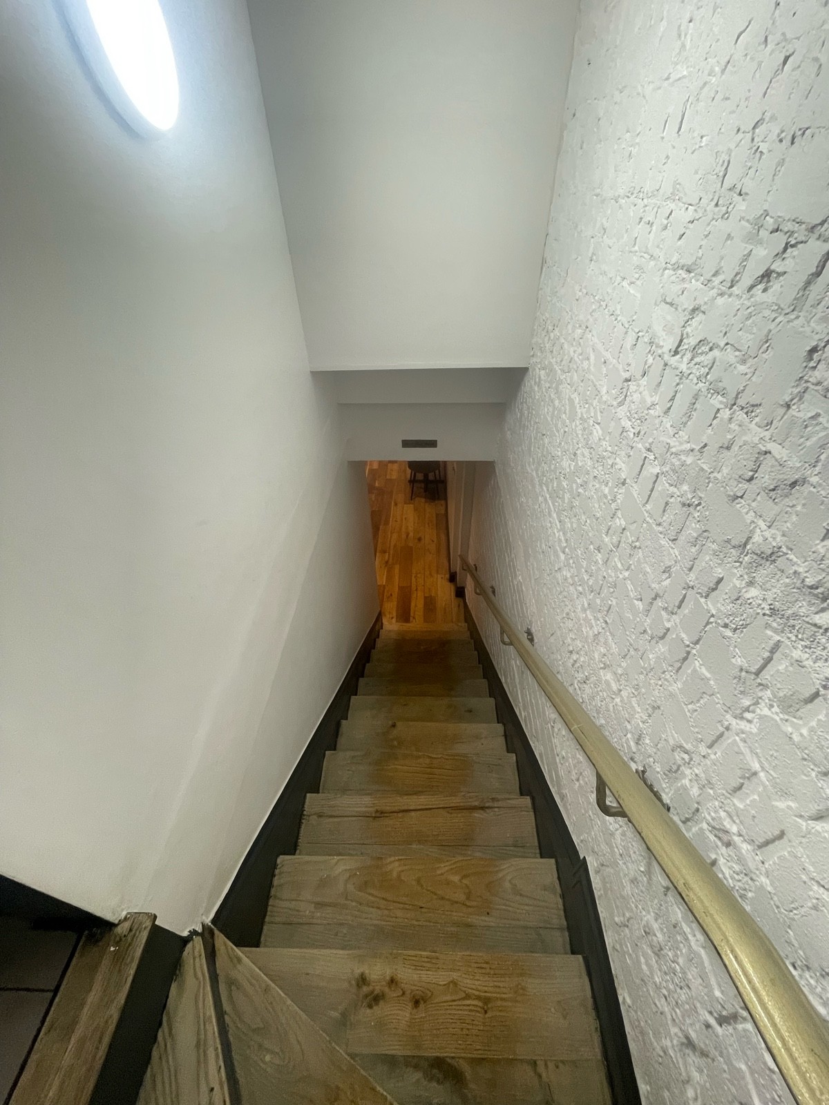 From second curved step facing left. Full flight of stairs down ahead. Gold metal handrail along right.