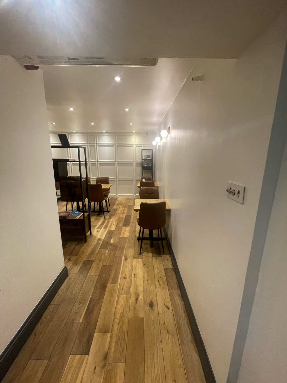 From bottom of stairs facing straight. Tables and chairs ahead to right. Metal book shelf ahead to left.