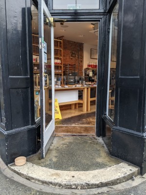 One step up to glass door with black frame and metal handle on right. Pull to open. Dog facilities on left at top of step.