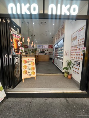 Glass doors with black metal frames fold open to left. A-frame sign obstructing on left of doorway.