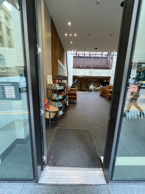 Glass door with grey metal frame and silver handle on right. Push to open.