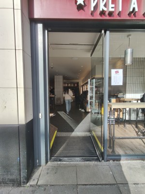 Grey framed glass door. Push grey handle on left to open. Doorbell for assistance on left.