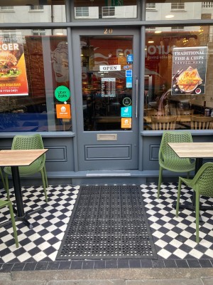 Path ahead between outdoors seating to entrance door on back. Glass door with grey frame. Push from right to open.