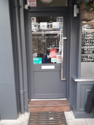 Grey door with glass panel. Push on right handle to open. One step up before door.