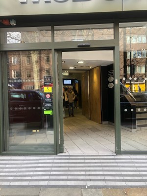 Glass doors with dark green frame. Slides from right to open. In-built ramp going up at foot of entrance.