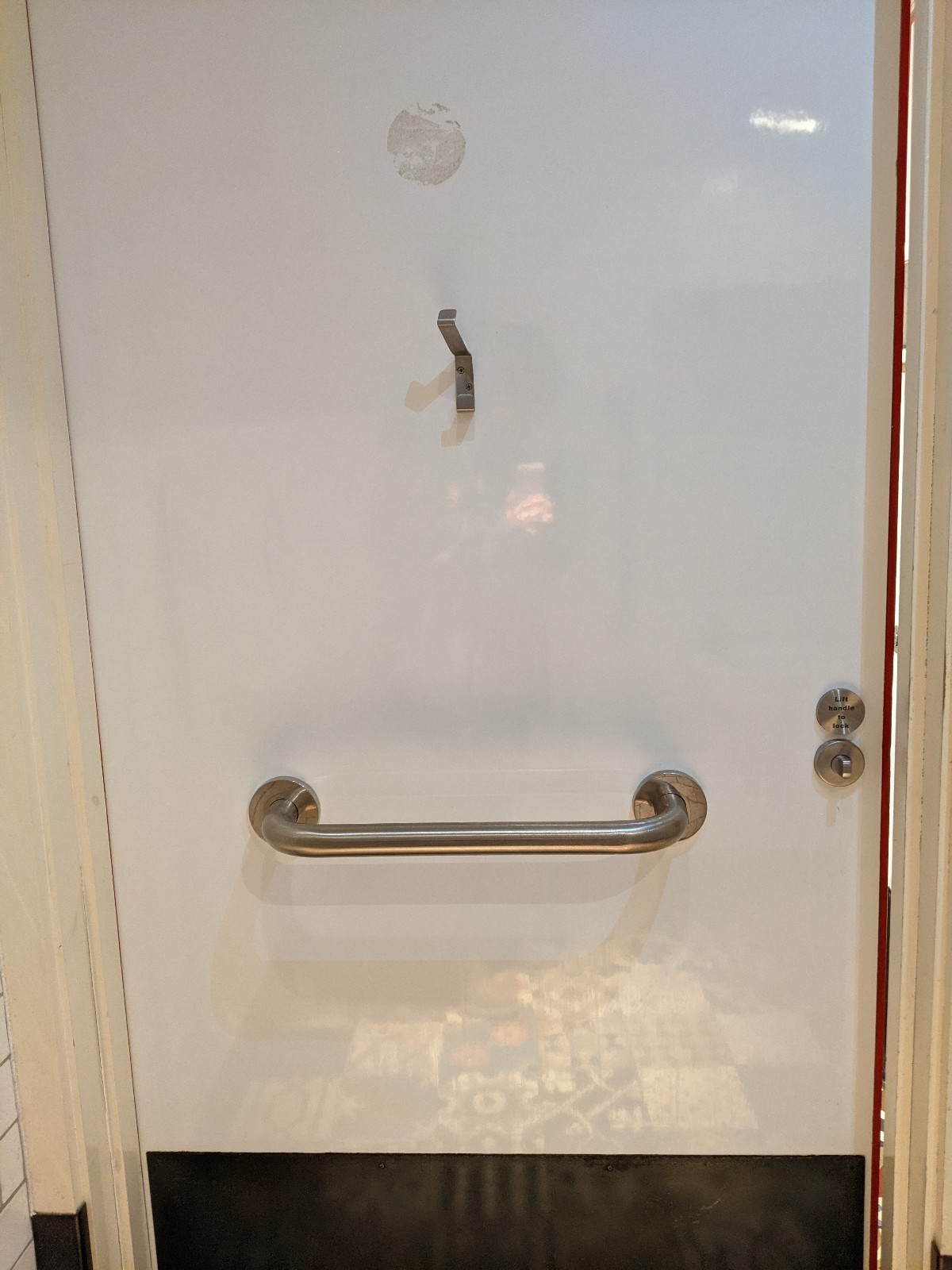 Back of toilet door. Grab rail mid centre, hanging hook above rail. Metal handle right of rail, push to open.