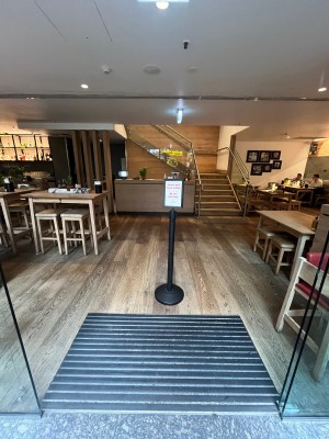 Glass doors slide open from middle. Signage obstructing ahead. Welcome desk on wall behind.
