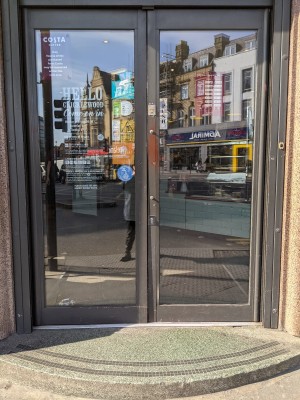 Glass doors with grey frame and metal handles in centre. Push to open.