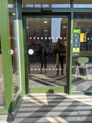 Glass door with green frame and no handle. Slides right to open.