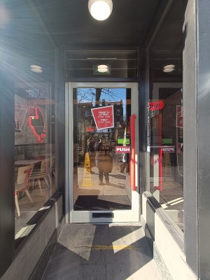 Glass door with silver, metal frame. Push red handle on right to open.
