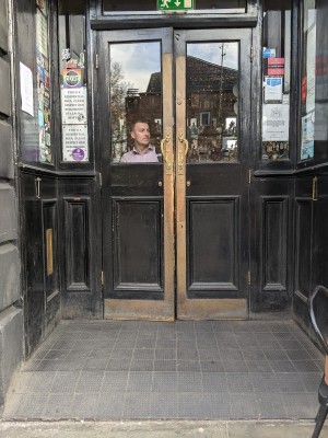 Small ramp before glass and black wood doors with metal handles in centre. Pull to open.