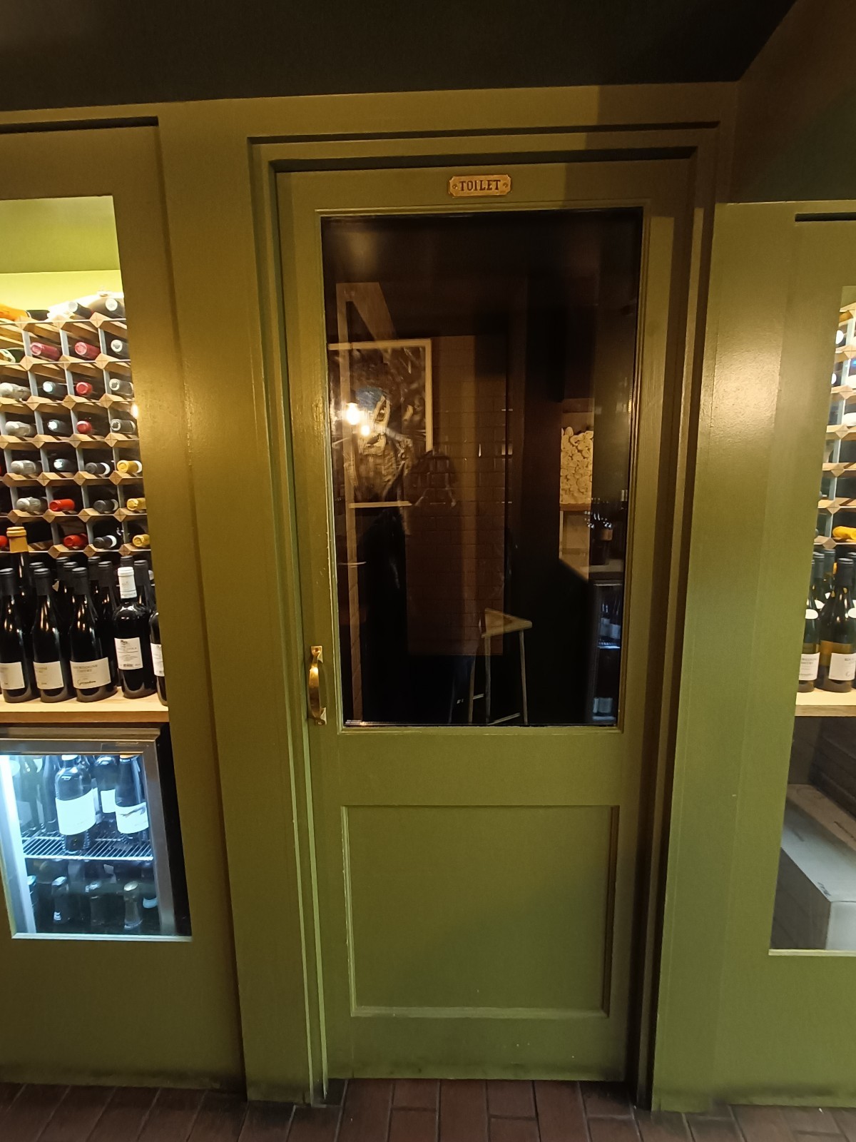 From left of downstairs area, looking left. Glass door with green wooden door ahead. Push golden handle on left to open.