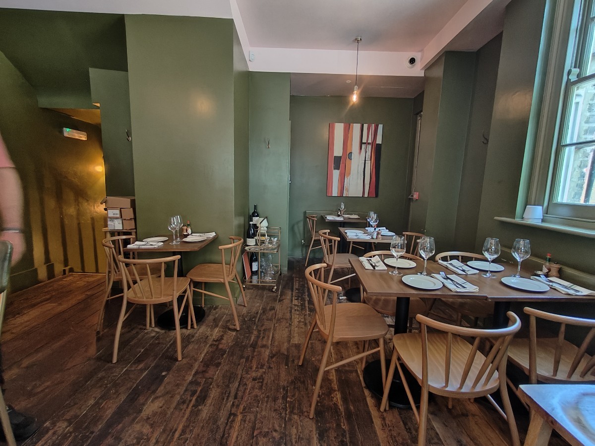 From end of open kitchen facing straight. Tables and chairs on left and along right.