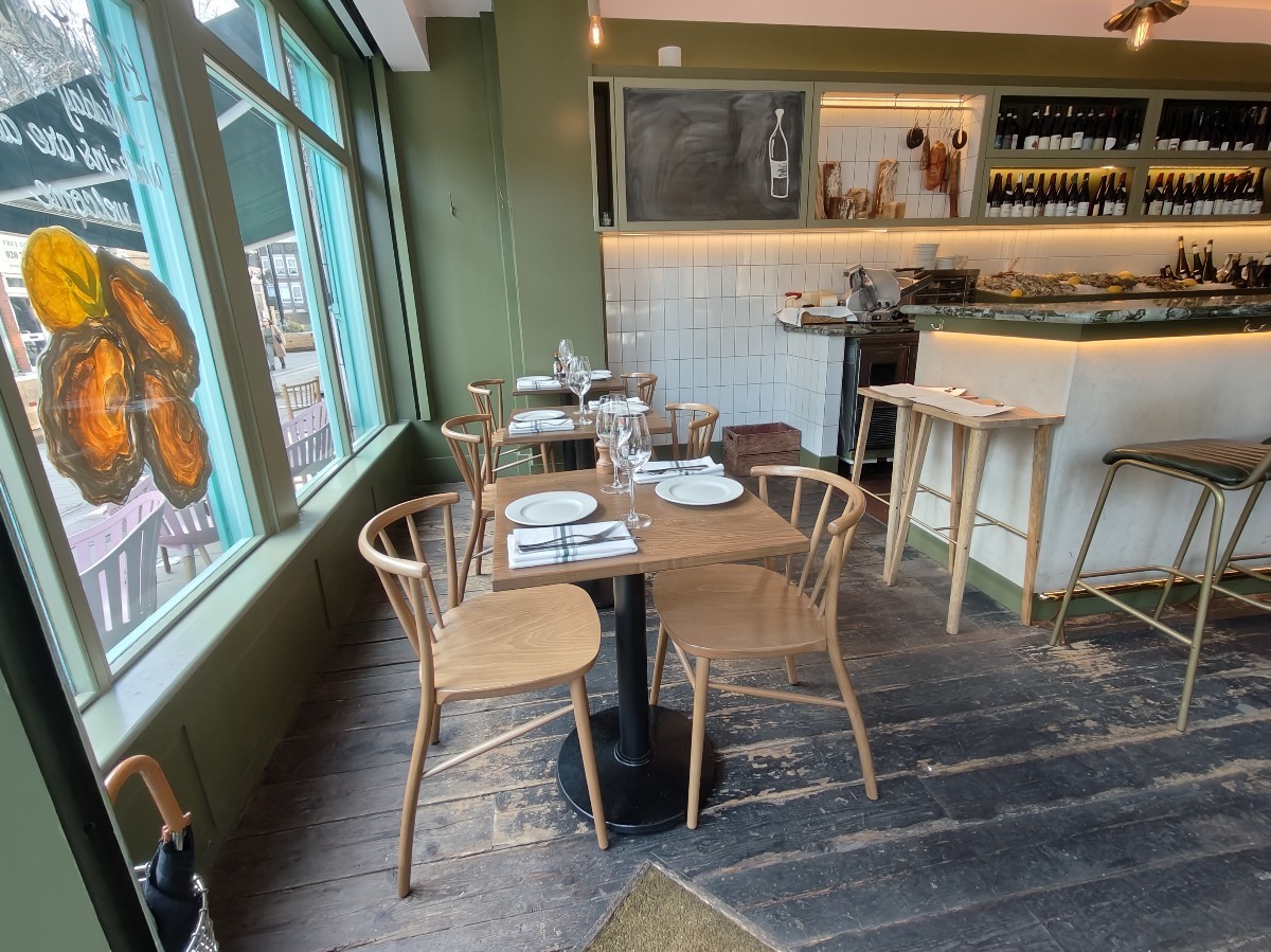 From entrance facing left. Tables and chairs ahead. Open kitchen and stools on right.