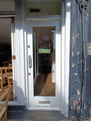 Glass door with white, wooden frame. Push silver handle on left to open.