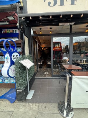 From pavement facing venue. Menu sign on left. Path in centre. Restaurant barrier on right.