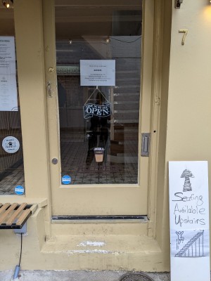 Glass door ahead with yellow frame and metal handle on left. Push to open.