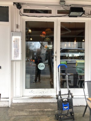 Glass door with white frame. Two steps up before door. Push metal handle on right to open.
