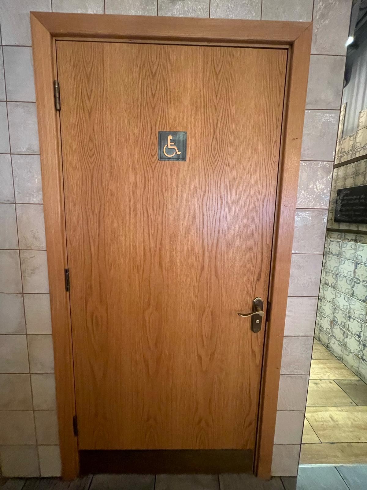From end of pathway facing straight. Brown wooden door ahead. Pull handle on right to open.