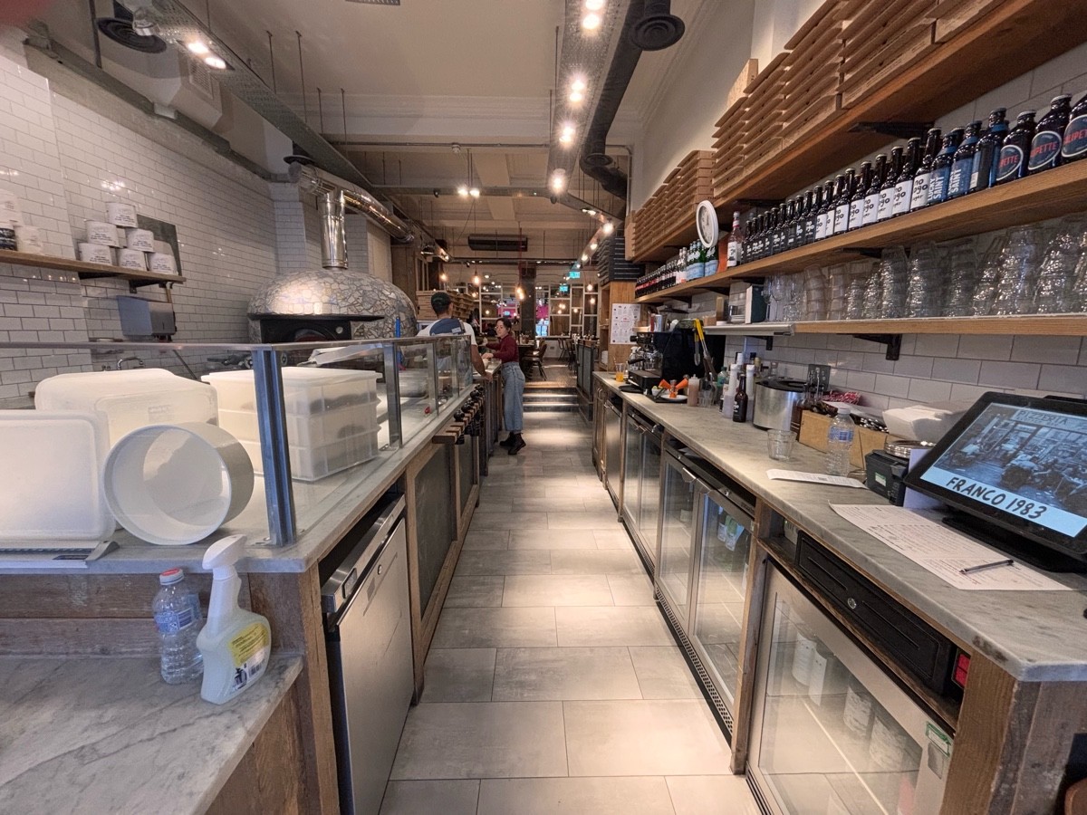 From end of condiment station facing left. Open kitchen along left. Product shelf along right, fridges below.