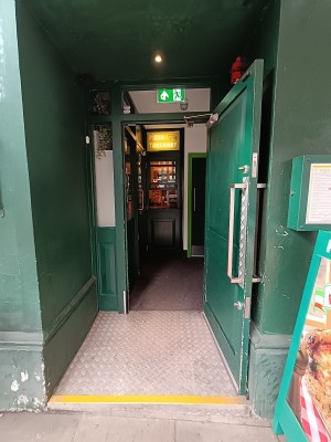 From street, facing venue. Green wooden door ahead. Pull silver handle on left to open.