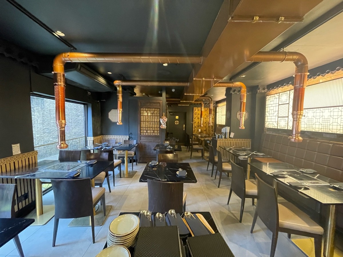 From top of steps facing straight. Tables and chairs in center space and on left. Half-booth and chairs on right.