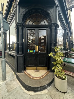 Black and glass panelled doors. Push from centre to open. Plant to right.