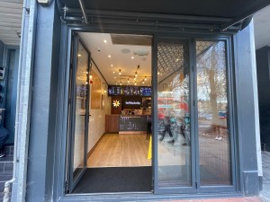 Facing glass door with black frame. Push black handle on right to open.