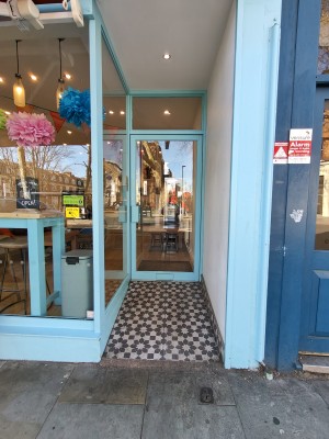 Glass door with blue, metal frame. Pull blue handle on left to open. Ramp up before doorway.