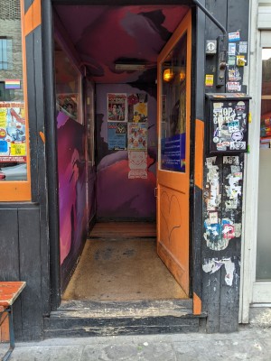 Glass door and orange wood door with metal handle on left. Push to open.