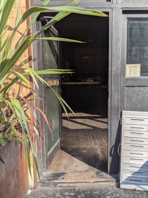 Glass door with black wood frame and black handle on right. Push to open.