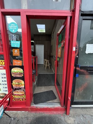 Glass door with red frames. Push from left to open. A step up at front of door. Built in ramp after.