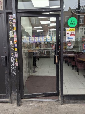 Glass door with black frame and metal handle on right. Push to open. Short ramp after door.
