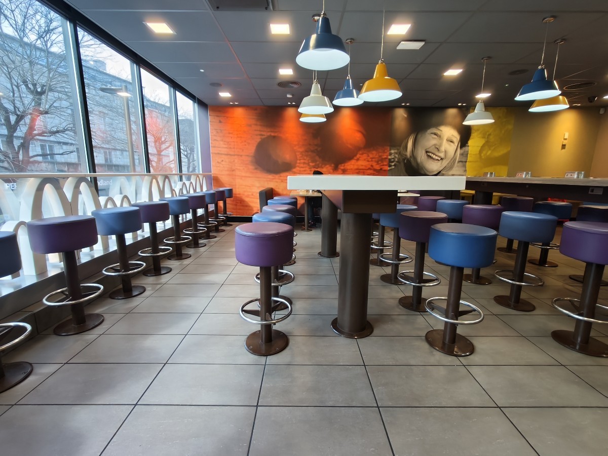 From end of half booths facing right. Rows of high tables and stools along left and centre. Booths behind.